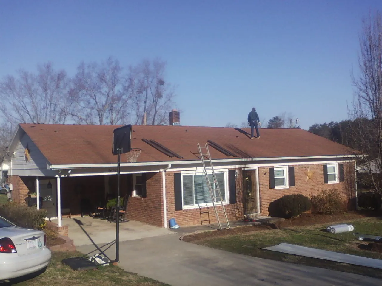 Roofer stripping a shingle roof on a brick ranch before metal panels in Grand Ridge
