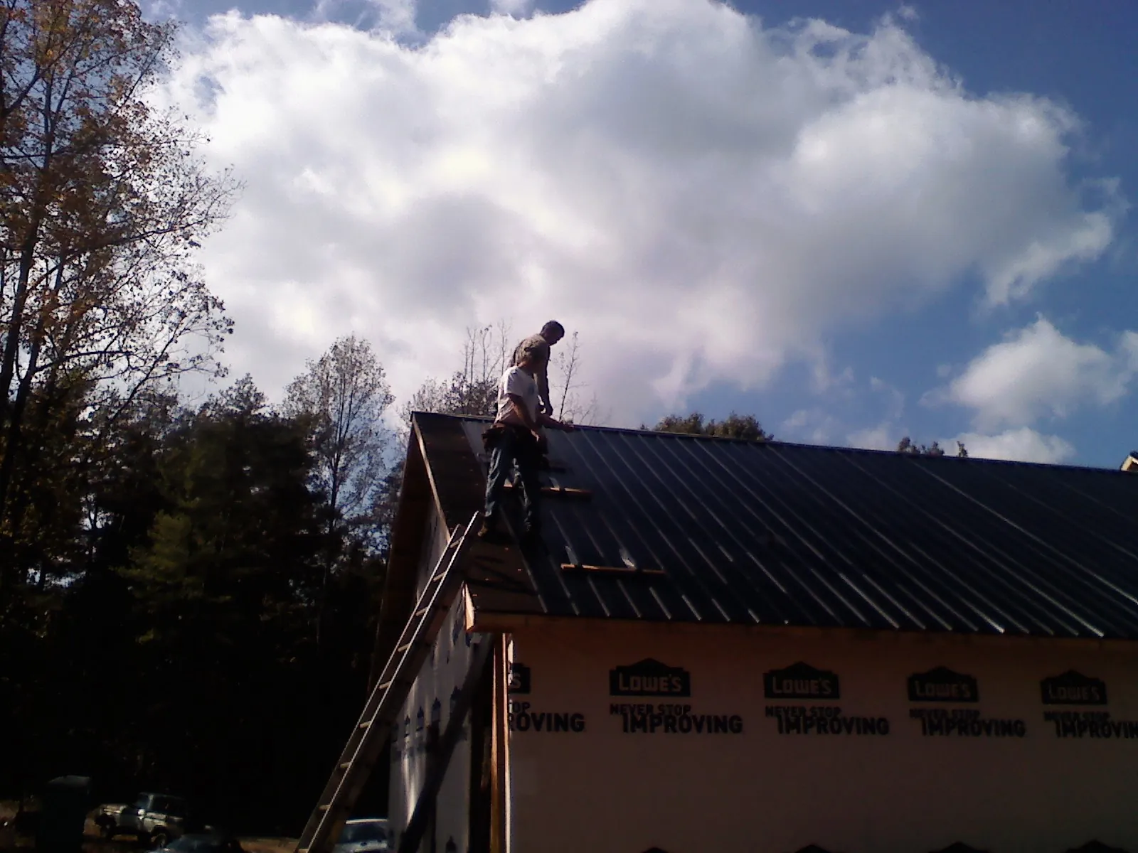 Roofer fastening dark metal panels high against a cloudy sky, from a Roof Inspection job in Grand Ridge