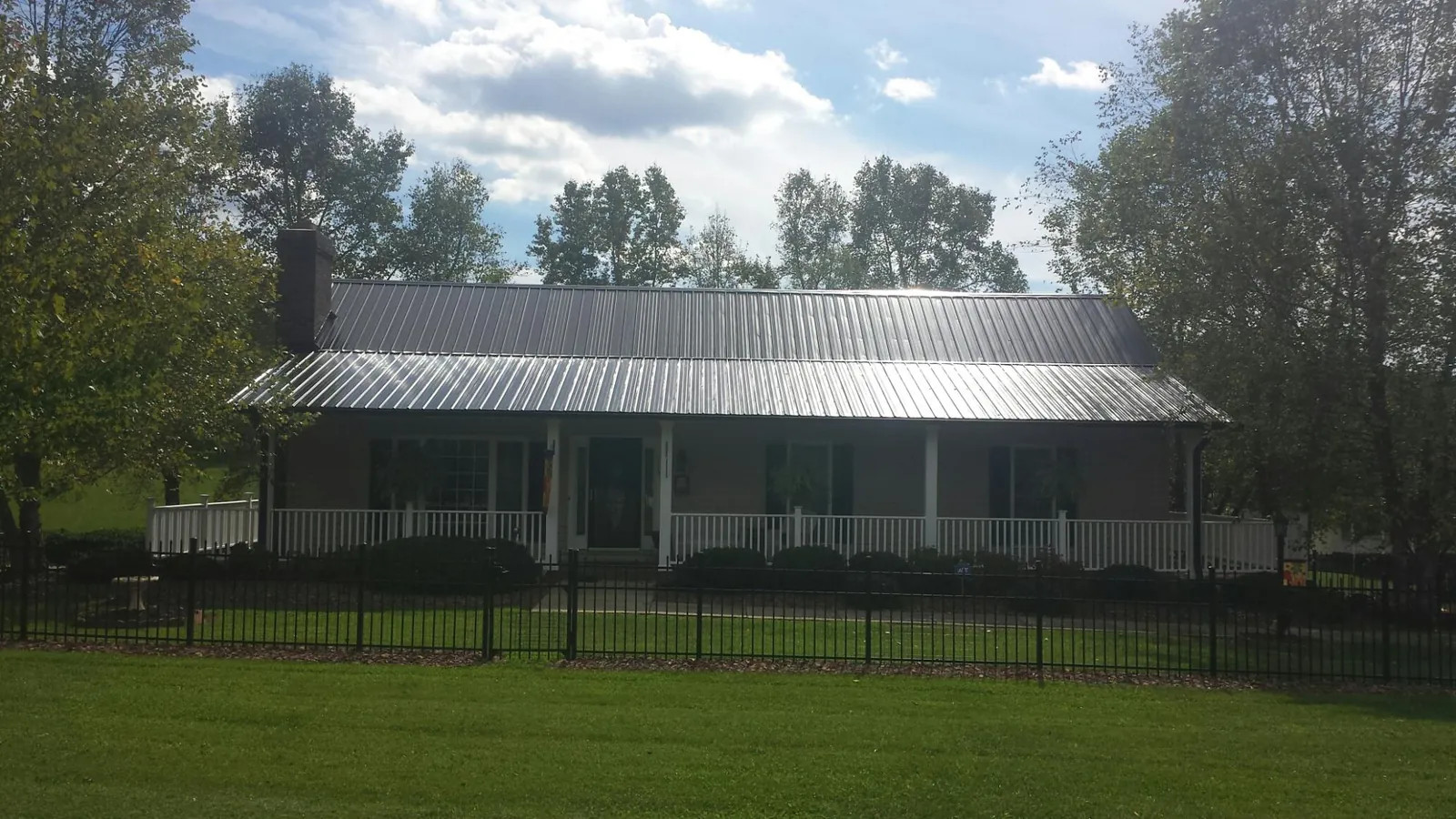 Gray metal roof on a brick ranch with a full width front porch — Gutter Guard Installation work by our crew in Grand Ridge