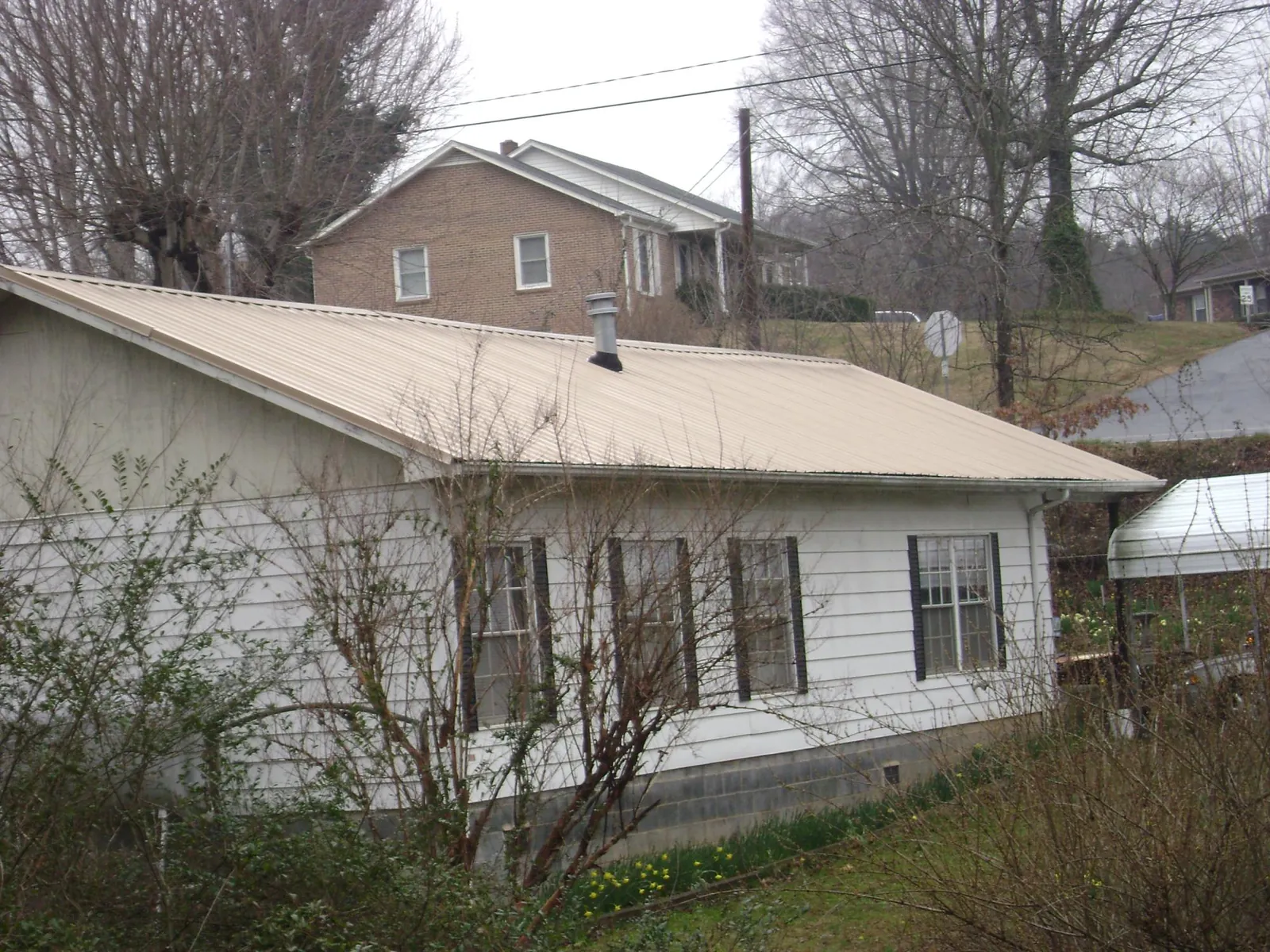 Tan metal roof on a white sided house set into a hillside — Commercial Roofing by Roofing Brothers in Grand Ridge